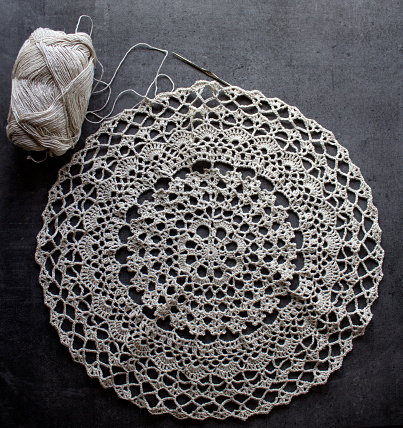 Eco Friendly decor element. Top view photo of crochet table cloth, ball of linen yarn and crochet hook. Dark grey background with copy space. Hobbies and crafts concept.