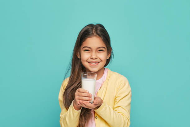 gosse féminin mélangé de course de verticale avec un verre de lait dans ses mains, isolé sur le fond turquoise. le lait est bon pour la santé des enfants - milk child drinking little girls photos et images de collection