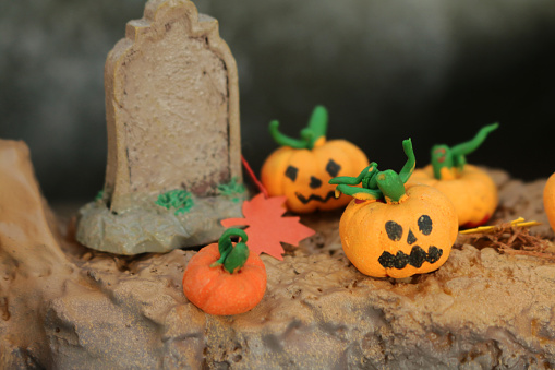 Stock photo showing seasonal holiday concept showing a creepy Halloween scene in miniature complete with homemade, orange, modelling clay pumpkins beside a miniature gravestone.