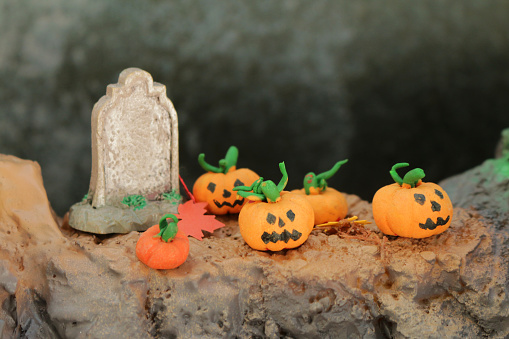 Stock photo showing seasonal holiday concept showing a creepy Halloween scene in miniature complete with homemade, orange, modelling clay pumpkins beside a miniature gravestone.