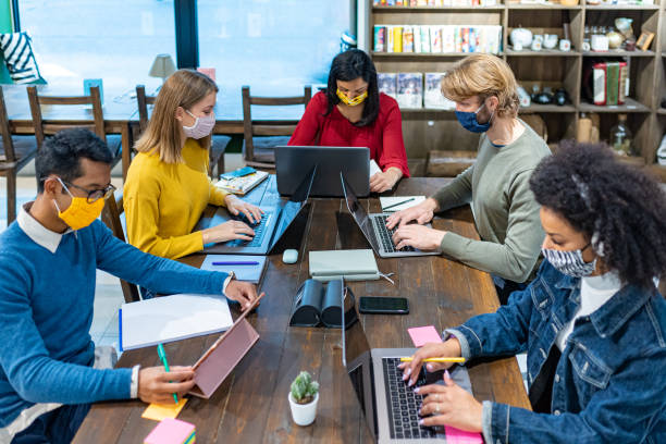 mitarbeiter in der tätigkeit in einem öffentlichen raum, gruppe kreativer junger menschen kooperieren für die geburt eines neuen start-ups, multiethnisches team mit gesichtsmasken arbeiten sicher, konzepte von vielfalt und inklusion - multi ethnic group reading stock-fotos und bilder