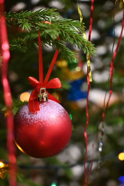 istock Red ball with ribbon bow hanging on decorated Christmas tree. Close-up. 1298302051