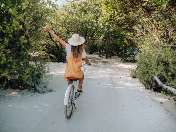 istock Young woman riding bicycle on white sand island 1298305961