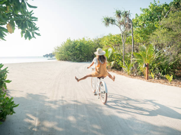 istock Young woman riding bicycle on white sand island 1298306199