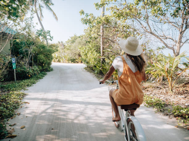 istock Young woman riding bicycle on white sand island 1298306995