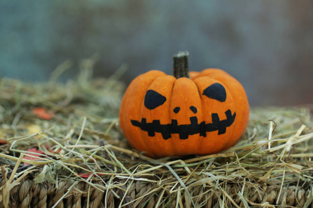 istock Image of pumpkin head scary Halloween face Jack O'Lantern on wicker shelf surrounded by hay pile 1298307775