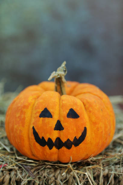 istock Image of pumpkin head scary Halloween face Jack O'Lantern on wicker shelf surrounded by hay pile 1298308476