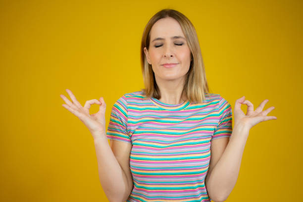 istock Young woman makes mudra sign, relaxes after hard working day, keeps eyes shut, practices yoga against yellow background. 1298309580