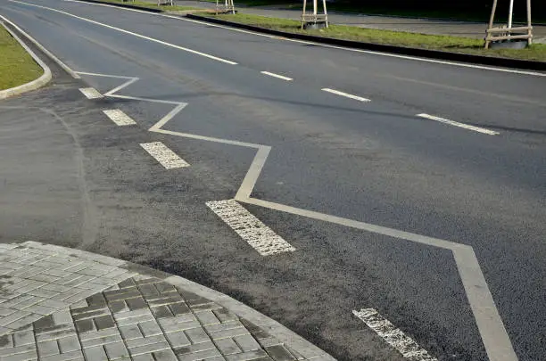 Photo of winding line on asphalt road at a turnoff at a side road junction. parking at these places is prohibited. concrete curbs and paving trees and lawn