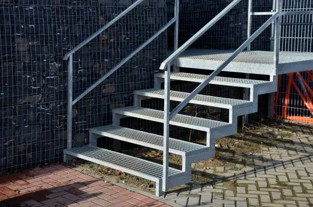 Photo of stair construction for car parks with high resistance to deformation even under heavy loads Welded floor grate made of galvanized steel and railings. concrete blocks and  wooden pole palisade