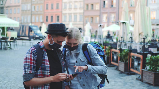 istock Young tourists in protective masks and with bags using smartphone 1298315064