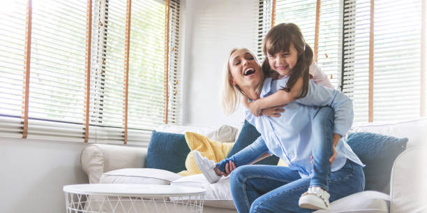 幸せな美しい母親が運ぶか、彼女の小さな娘を笑って、ソファで一緒に楽しんで - family indoors happiness laughing ストックフォトと画像