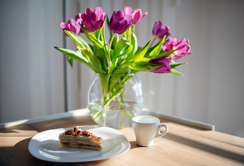 Handmade cake with nuts and the smell of morning coffee arranged with bouquet of beautiful violet tulips in glass vase.