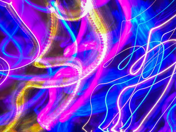 Curving light trails in an ornamental garden with holiday illumination at night. Long exposure with motion blur. Light painting.