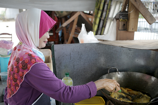 A Muslim woman is frying banana fritter at her business stall.