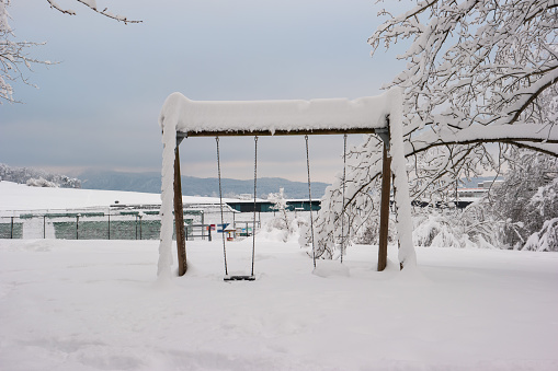 Snowy playground in the forest with snow covered swing and trees in Switzerland.