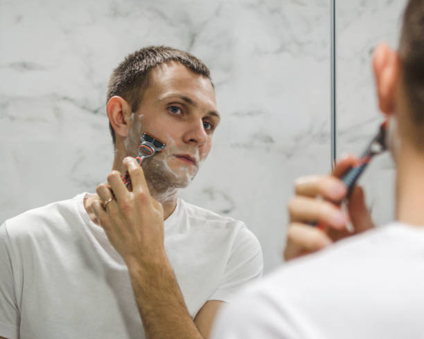 istock a young man is shaving his beard near the mirror 1298323717