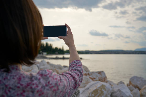 istock Woman's hands holding a smartphone and make photo during sunset on the lake. 1298326328