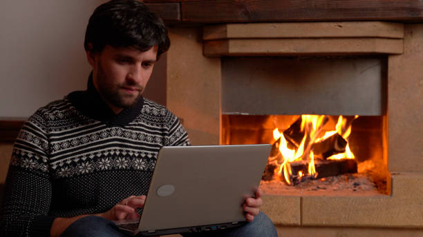 istock Woman using a digital laptop sits by the fireplace 1298326386