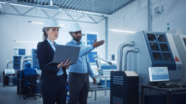 istock Modern Factory with Professional Workers, Engineers, Managers Working on Production Line, Workshop Management, Optimization. Industrial Facility: Equipped with CNC Machinery and robot arm Technology 1298326662