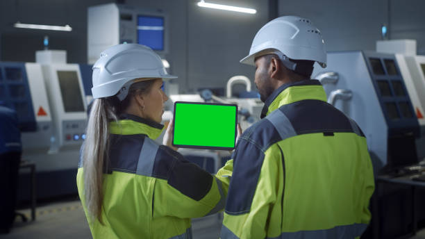 industria 4.0 fabbrica: ingegnere capo e supervisore del progetto in giubbotti di sicurezza e cappelli duri, talk, usa tablet computer digitale con schermo verde, chiave chroma. officina con macchinari. - sagoma prodotto foto e immagini stock