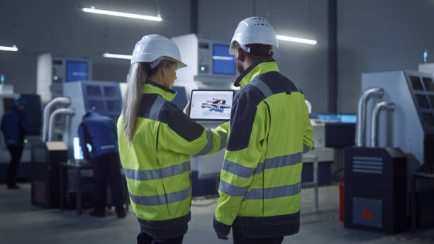 istock Industry 4.0 Factory: Chief Engineer and Project Supervisor in Safety Vests and Hard Hats, Talk, Use Digital Tablet, Screen Shows 3D Concept of New Jet Engine. Industrial Workshop with Machinery. 1298326713