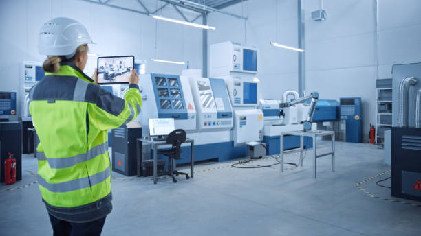 istock Industry 4.0 Modern Factory: Female Engineer Uses Digital Tablet Computer with Augmented Reality to Visualize Workshop Mapping, Floor Layout. Facility with High-Tech CNC Machinery and robot arm 1298326738