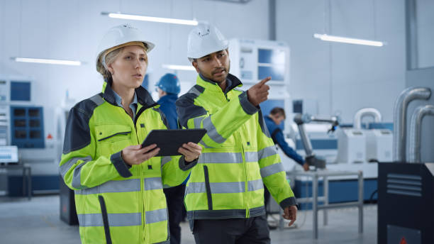 istock Chief Engineer and Project Supervisor in Safety Vests and Hard Hats Walk Through Modern Factory, Talking, Optimizing Production. Industrial Facility: Professionals Use Machinery. 1298326748
