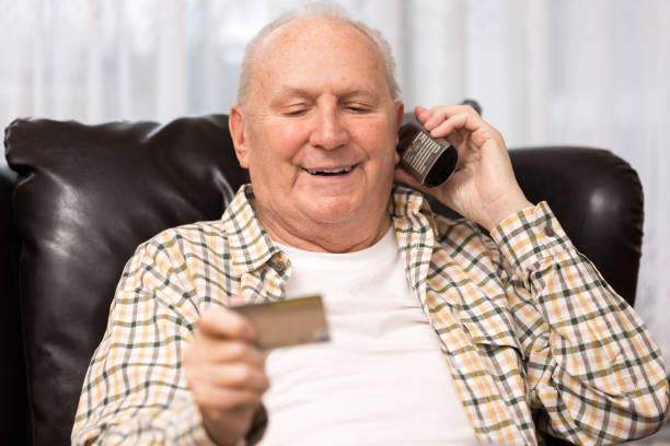 istock Senior man holding credit card while using the phone at home 1298327901