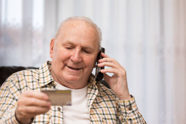 istock Senior man holding credit card while using the phone at home 1298327914