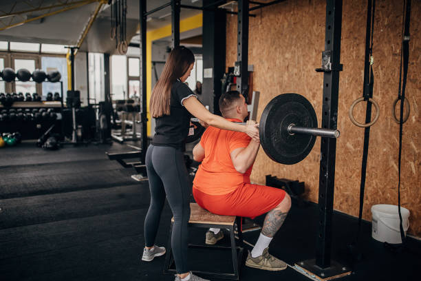 istock Female personal trainer assisting a man in weightlifting exercise 1298327950