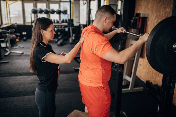 istock Female personal trainer assisting a man in weightlifting exercise 1298328128