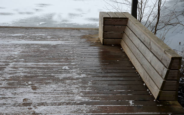 posti a sedere in legno con panchine rivestite in legno naturale nei boschi vicino all'acqua. terrazza sul ponte vicino allo stagno. tutto è un pezzo con articolazioni in inverno con un albero di neve nel buco del palco - non urban scene landscaped winter snow foto e immagini stock