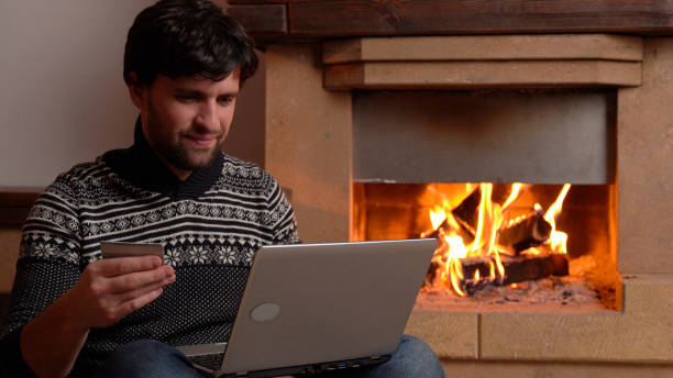 istock Man shopping online using laptop at home sitting by the fireplace 1298329567