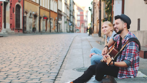 istock Tourists sitting on sidewalk, playing guitar and having rest 1298330099