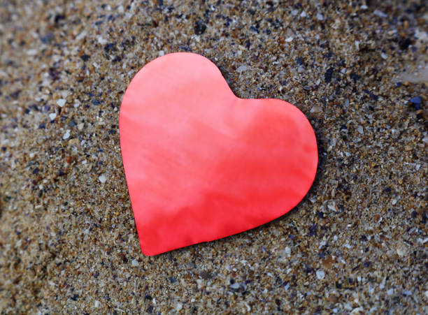 istock Shiny red paper heart on the sand. 1298331142