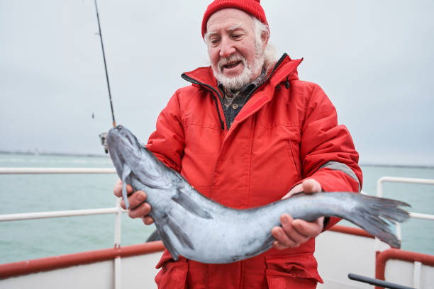 istock Senior man holding fish while standing at the boat 1298331691