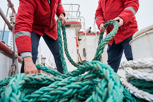 Close up view of a two male colleagues fishermans pulling rope on deck of a boat at the cold winter day. Occupation concept. Stock photo