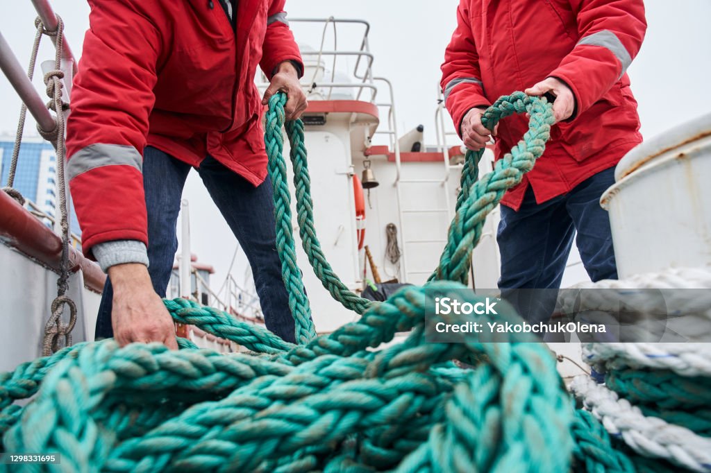 Two male colleagues fishermans pulling rope on deck of a boat Close up view of a two male colleagues fishermans pulling rope on deck of a boat at the cold winter day. Occupation concept. Stock photo Boat Deck Stock Photo