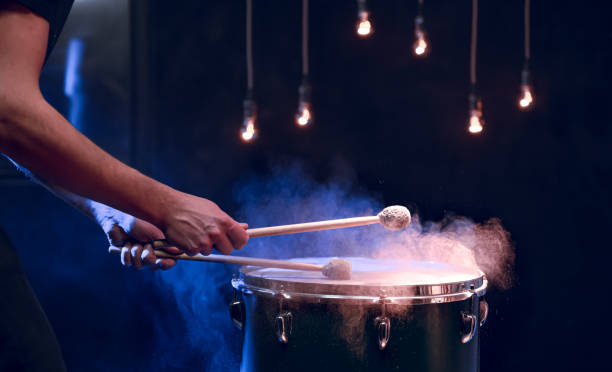 The drummer plays with mallets on floor tom in dark room. The percussionist plays with sticks on the floor tom on under studio lighting.. Concert and performance concept. snare drum stock pictures, royalty-free photos & images
