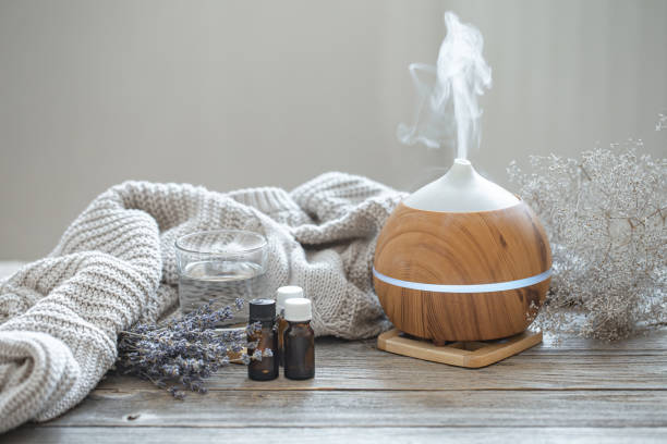 Composition with an air humidifier and a set of aromatic oils. Modern aroma oil diffuser on wood surface with knitted element, water and oils in jars. aromatherapy photos stock pictures, royalty-free photos & images