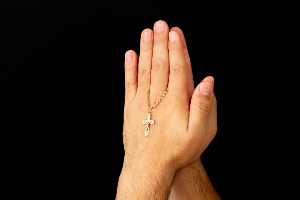 Young male hands with christian cross praying to God at church Young male hands with christian cross praying to God at church on dark background orthodox church easter stock pictures, royalty-free photos & images