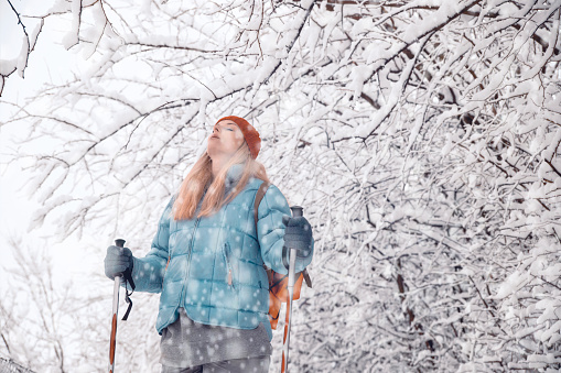 Woman breathing fresh cold air on hiking in winter snowy day outdoors. Enjoying snowfall walking in the woods. Copy space