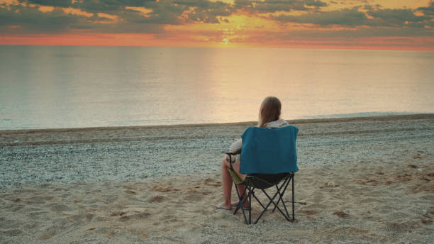 istock Woman sitting on camping chair and drinking coffee 1298345193