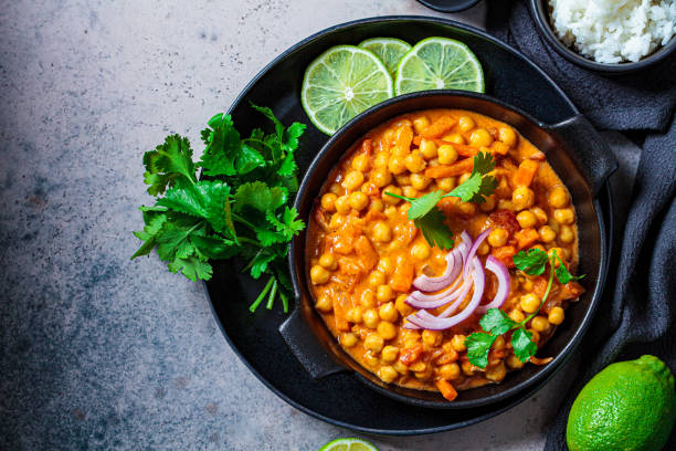 curry di ceci vegano con riso e coriandolo in piatto nero, sfondo scuro. concetto di cucina indiana. - curry sauces foto e immagini stock