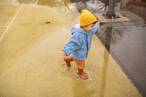 Little boy having fun in puddle in schoolyard