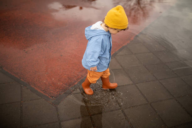 istock Child in rubber boots walking over puddle during autumn day 1298349880