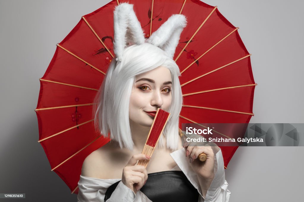 Blonde girl in a wig on a gray background with an umbrella, cosplay cat women. Cosplay Stock Photo