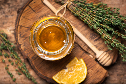 Jar of honey with thyme leaves bunch on rustic table top view