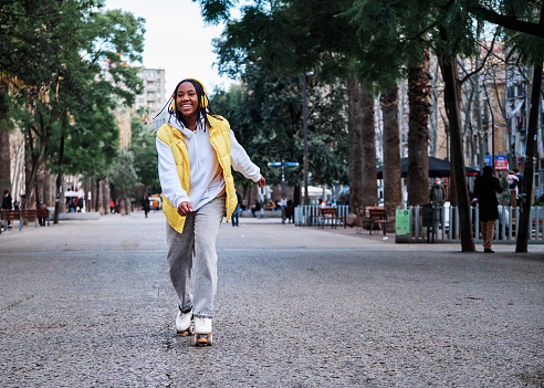 African american woman smiling and listening music with headphones while roller skating outdoors on the street. Urban concept.